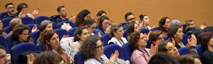 Numerosos asistentes sentados en un auditorio aplauden durante la celebración de un acto o conferencia. El público, compuesto principalmente por mujeres y hombres jóvenes y adultos, ocupa las butacas azules de la sala mostrando su participación activa en el evento.